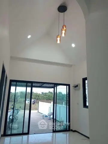 Spacious living room with high ceiling and large glass doors opening to a scenic view.