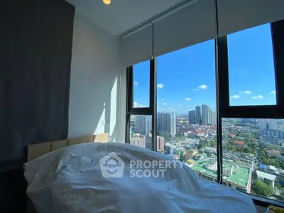 Stunning bedroom with panoramic city view from high-rise window, featuring cozy bedding and abundant natural light.