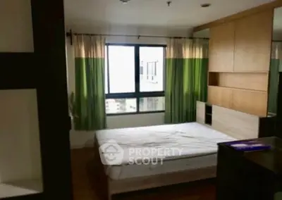 Spacious bedroom with large window and modern furnishings in urban apartment.
