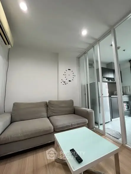 Modern living room with sleek kitchen, featuring a cozy gray sofa and glass partition.
