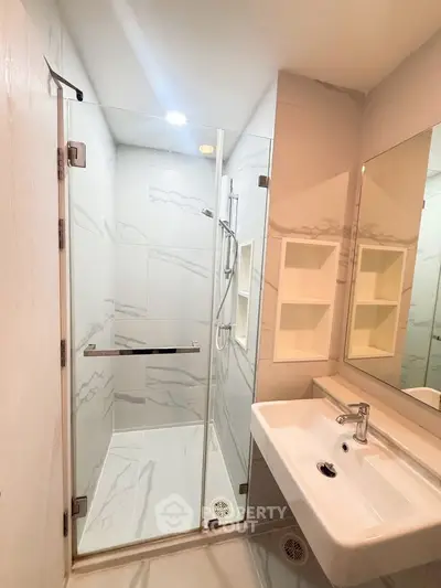 Modern bathroom with glass shower and sleek white sink in contemporary apartment.