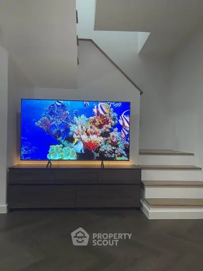 Modern living room with stylish staircase and large TV displaying vibrant coral reef.