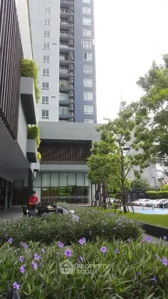 Modern high-rise building with lush garden and outdoor seating area.