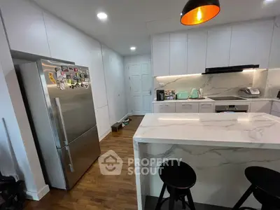Modern kitchen with sleek white cabinets and marble island, featuring stainless steel appliances and hardwood floors.