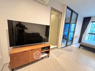 Modern apartment interior with TV, wooden cabinet, and bedroom view