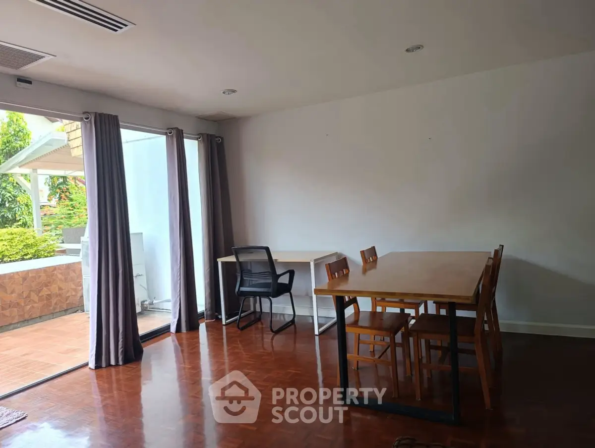 Spacious dining area with wooden flooring and garden view balcony access.