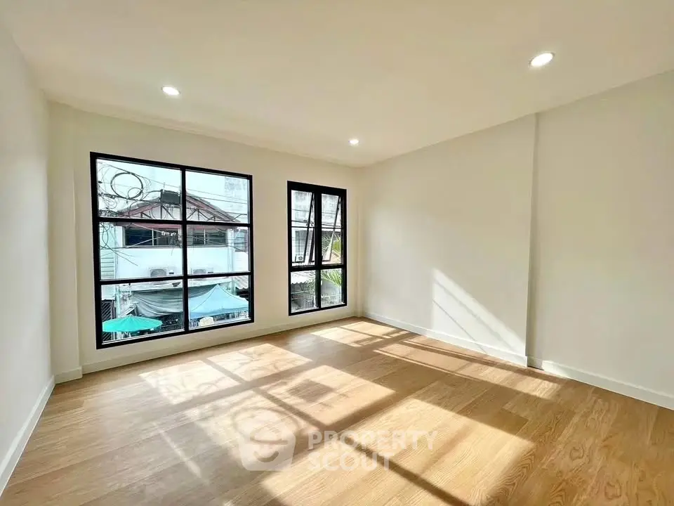 Bright and spacious room with large windows and wooden flooring, perfect for modern living.