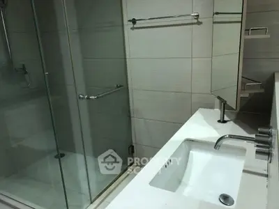 Modern bathroom with glass shower and sleek white sink in contemporary design.