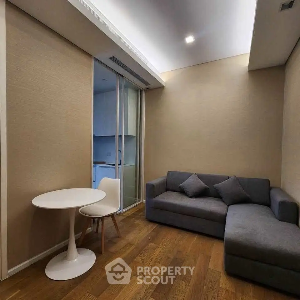 Cozy living room with modern gray sofa and small dining area, featuring wooden flooring and neutral walls.