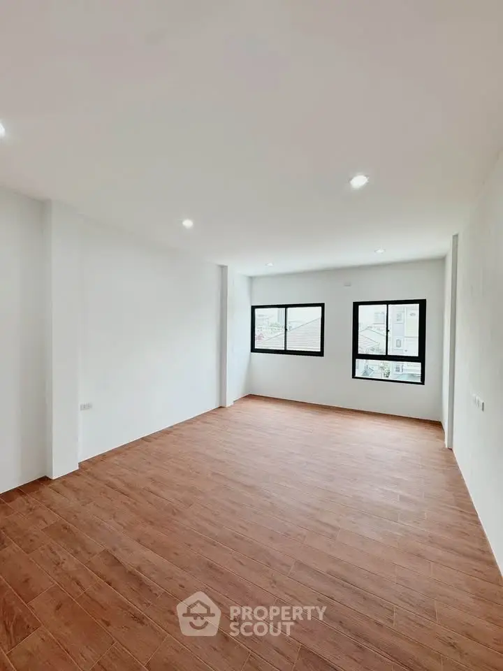 Spacious empty room with wooden flooring and large windows, perfect for customization.