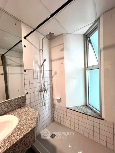 Modern bathroom with sleek shower and granite countertop in bright natural light.