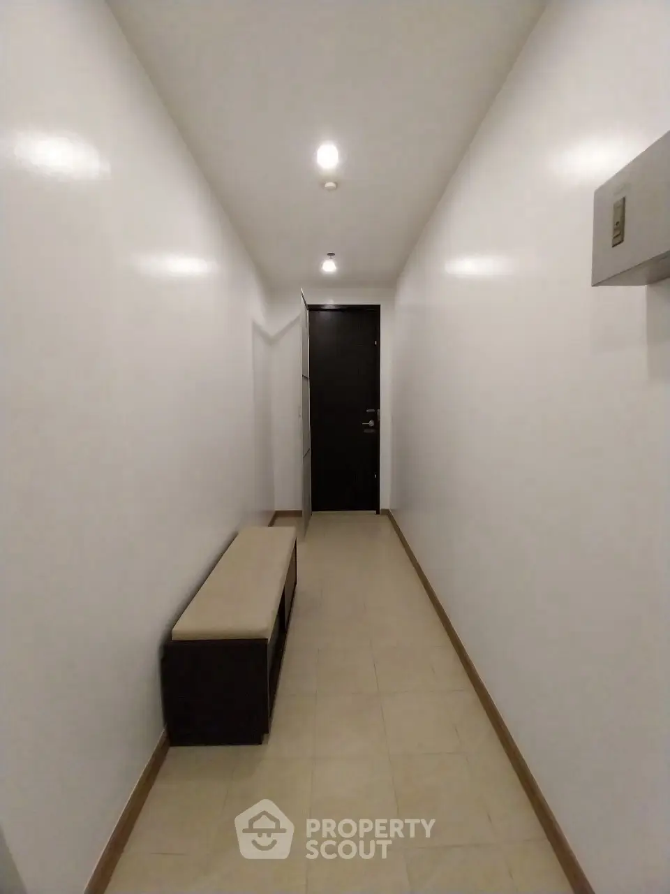 Minimalist hallway with bench and modern lighting leading to a sleek black door.