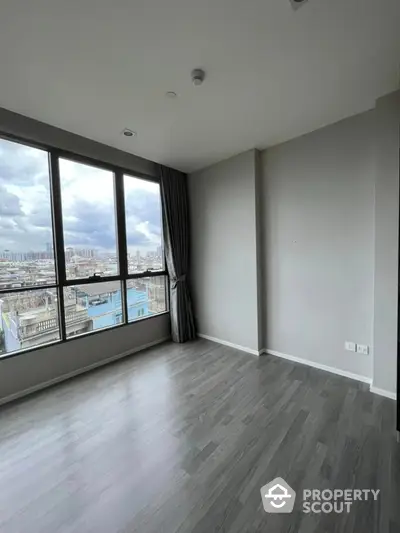 Spacious empty room with large windows offering stunning city views and modern flooring.