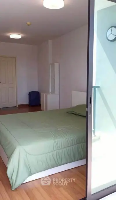 Spacious bedroom with green bedding and natural light, featuring a modern design and wooden flooring.
