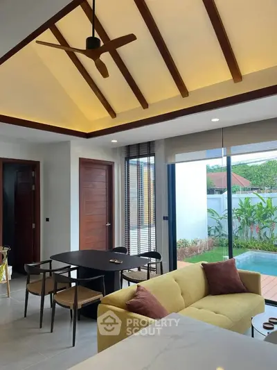 Modern living room with vaulted ceiling and pool view, featuring stylish furniture and open layout.