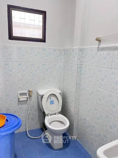 Compact bathroom with blue tile flooring and patterned wall tiles, featuring a toilet and small window.