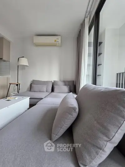 Modern living room with sleek gray sofa and large windows offering natural light.