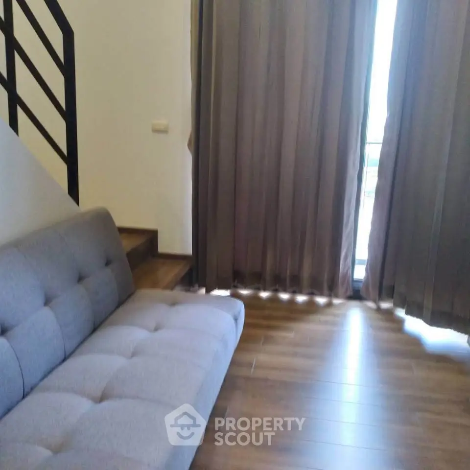 Modern living room with stylish sofa and wooden flooring, featuring large windows with elegant curtains.