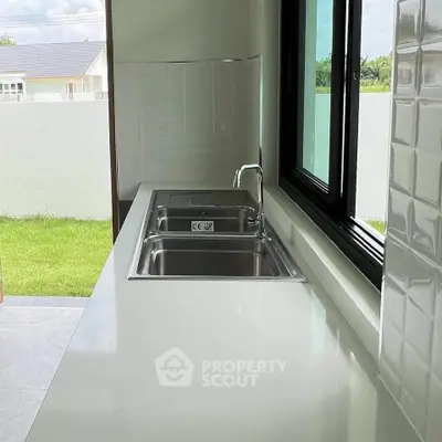 Modern kitchen with sleek countertop and stainless steel sink overlooking a lush garden view.