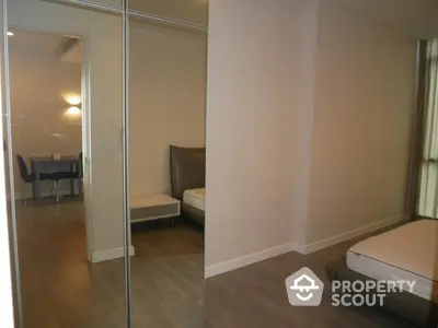 Spacious bedroom with mirrored closet doors reflecting a well-lit dining area, offering a modern and sleek living space.