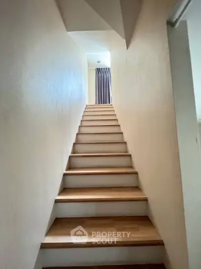 Modern staircase with wooden steps leading to a bright upper floor.