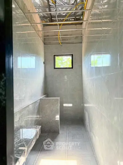 Modern bathroom with sleek gray tiles and small window, under construction.
