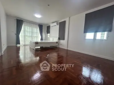 Spacious bedroom with polished wooden floors and large windows for natural light.