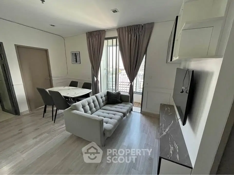 Modern living room with stylish decor, featuring a cozy sofa, dining area, and large window with balcony access.