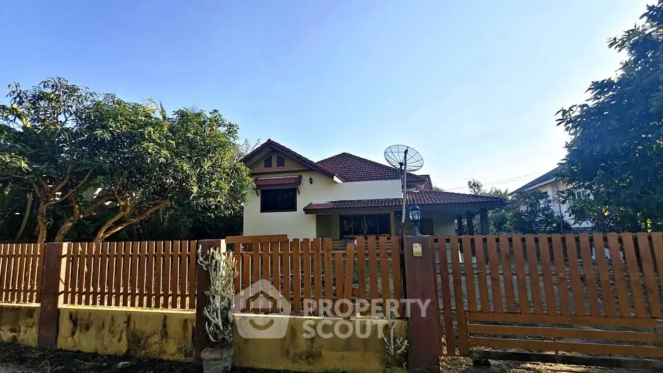 Charming single-story house with red-tiled roof and wooden fence in a lush garden setting.
