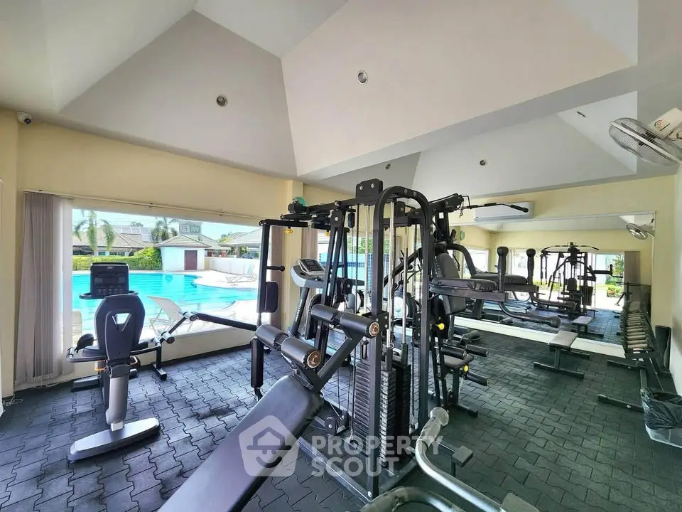 Spacious gym with modern equipment and pool view in luxury real estate property.