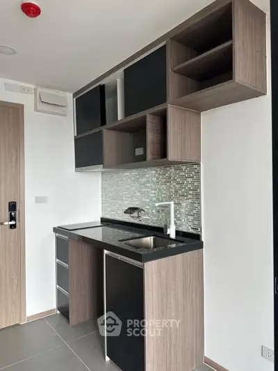 Modern compact kitchen with sleek cabinetry and stylish backsplash in a contemporary apartment.