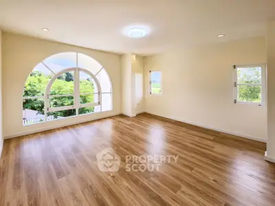 Spacious empty room with large arched window and wooden flooring
