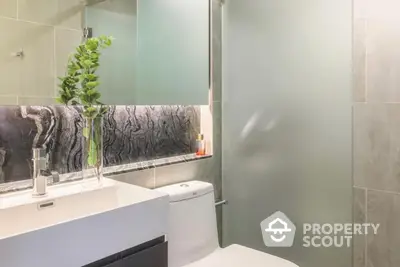 Modern bathroom with sleek finishes, featuring a large mirror, under-sink storage, and a touch of greenery for a serene ambiance.