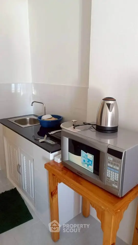 Compact kitchen with microwave, kettle, and sink in a cozy apartment.
