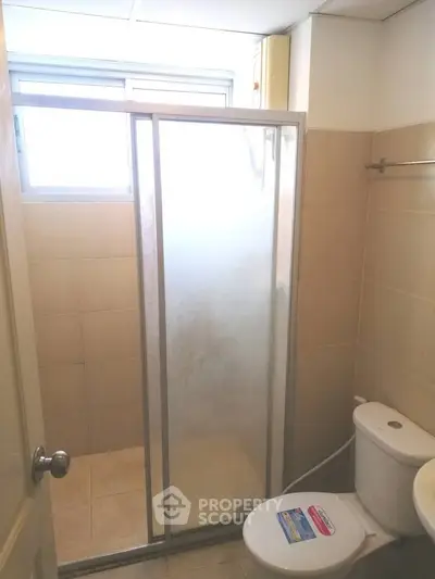 Compact bathroom with shower enclosure and toilet in a bright setting.