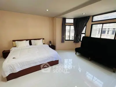 Spacious bedroom with large windows and modern furnishings in a well-lit apartment.