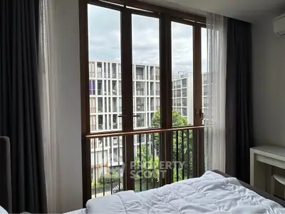 Modern bedroom with large window offering a view of contemporary apartment buildings.