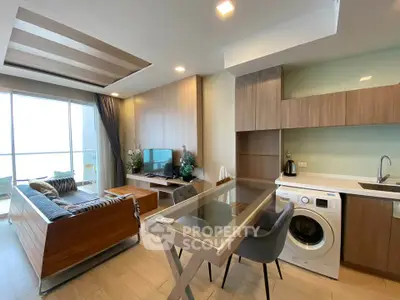 Modern living room with open kitchen, featuring a washing machine and stylish wooden furniture.