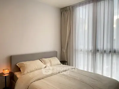Cozy bedroom with soft lighting and large window draped with sheer curtains.