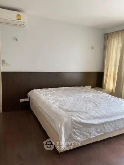 Spacious bedroom with modern design and natural light, featuring a comfortable bed and elegant wooden flooring.