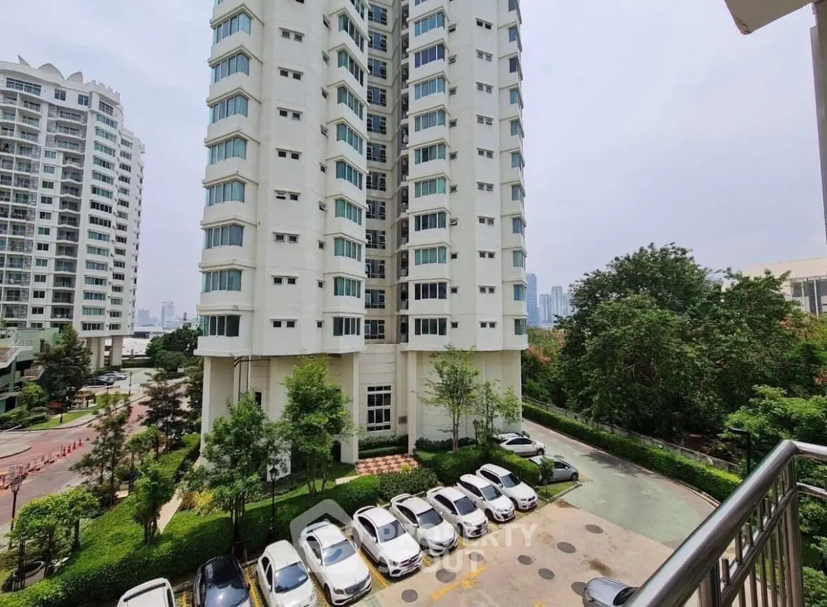 Modern high-rise building with lush greenery and ample parking space in urban setting.