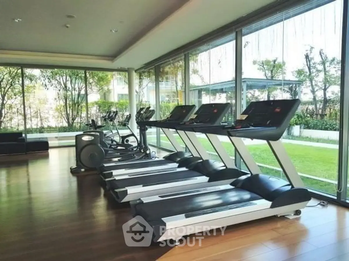 Modern gym with treadmills and large windows overlooking a lush garden.