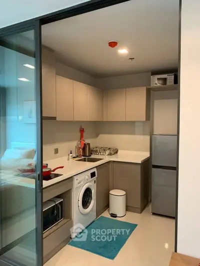 Modern kitchen with washing machine and sleek cabinetry in compact apartment.