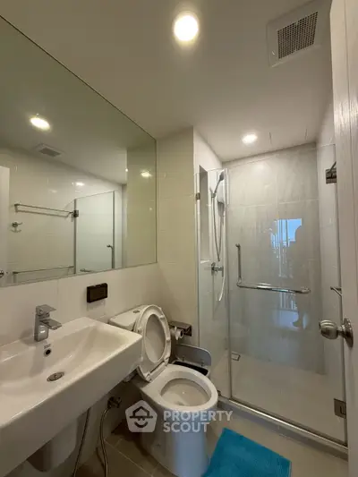 Modern bathroom with glass shower, sleek sink, and bright lighting in a contemporary apartment.