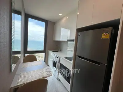 Modern kitchen with ocean view, sleek appliances, and dining area in high-rise apartment.