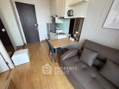 Modern compact living room with kitchenette, featuring sleek furniture and wooden flooring.