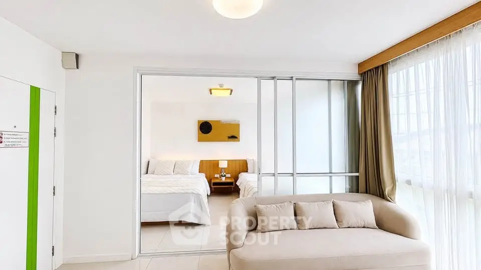 Modern living room with cozy sofa and sliding doors leading to a bright bedroom.