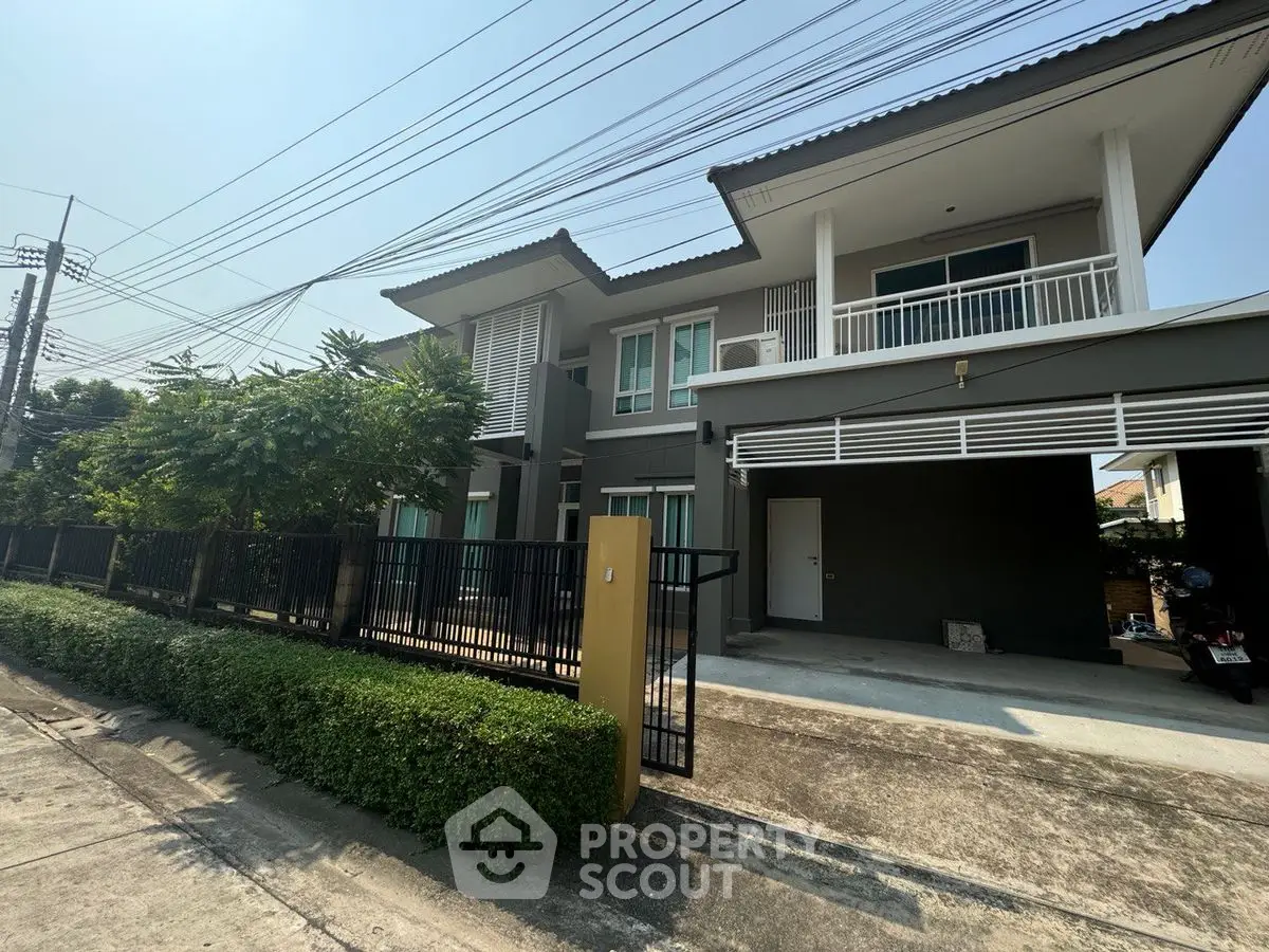 Modern two-story house with spacious balcony and lush greenery in a serene neighborhood.