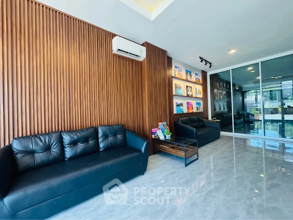 Modern living room with sleek black sofas, wooden paneling, and glass wall for a contemporary touch.