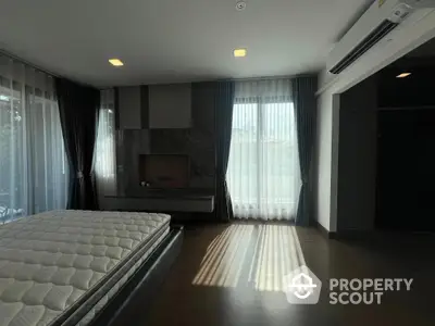 Spacious bedroom with modern design, featuring a large bed, elegant dark wood accents, and ample natural light filtering through sheer curtains.